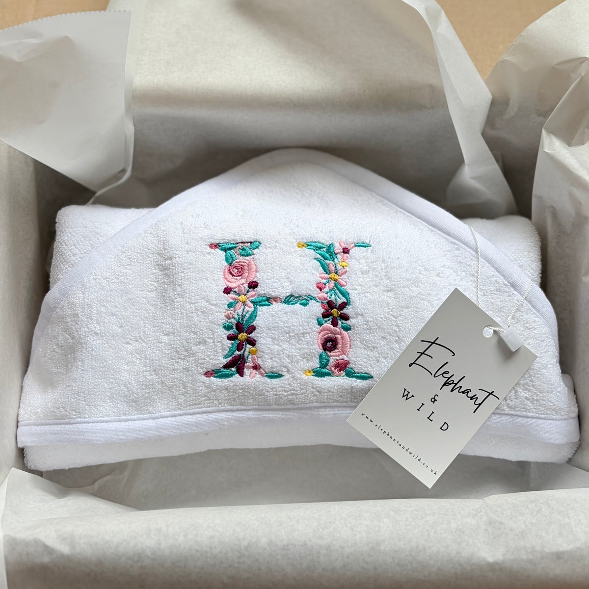 White personalised baby towel featuring a colourful Pink floral letter H embroidered in pink and turquoise.
