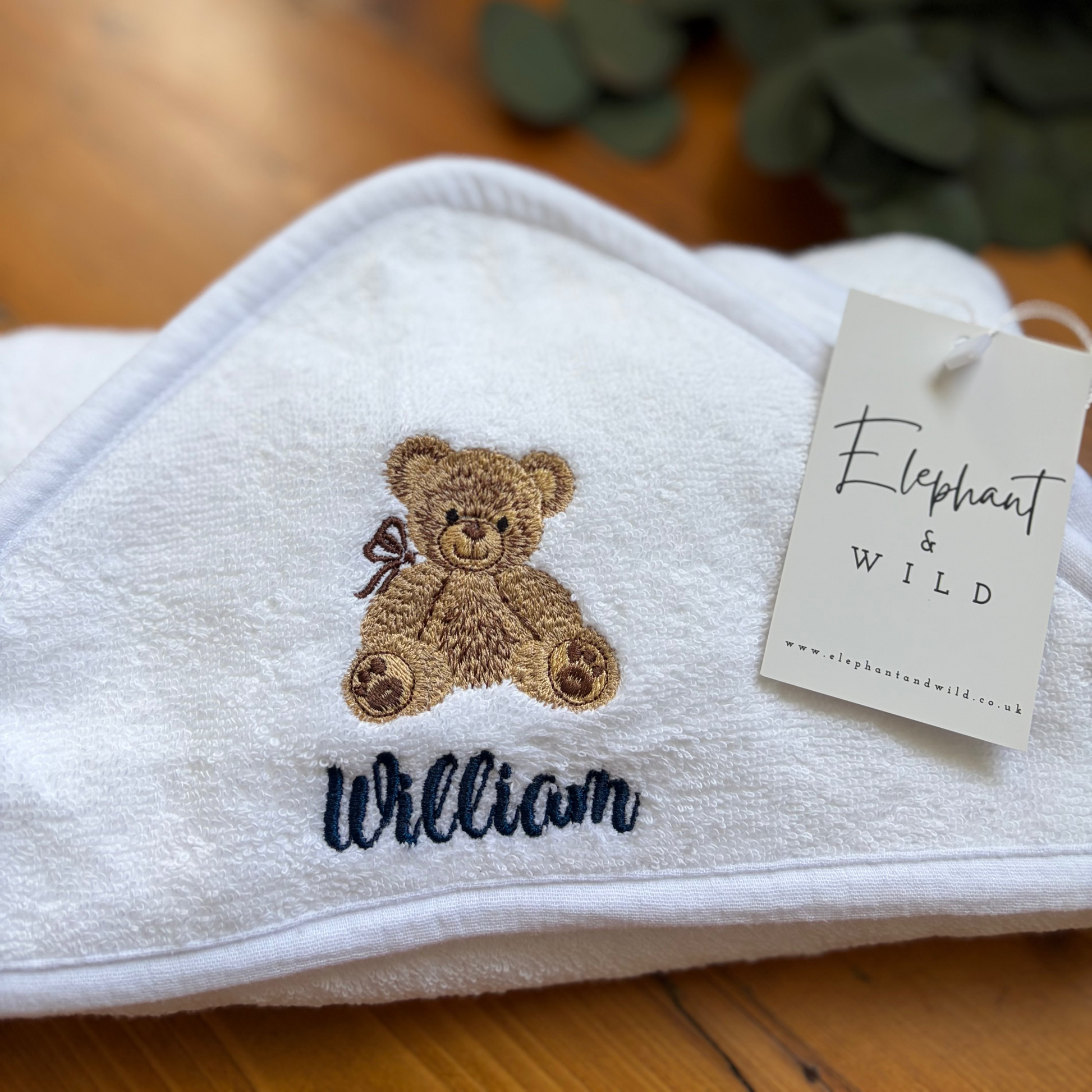 White personalised hooded baby towel embroidered with the name William in navy blue and a teddy bear design.